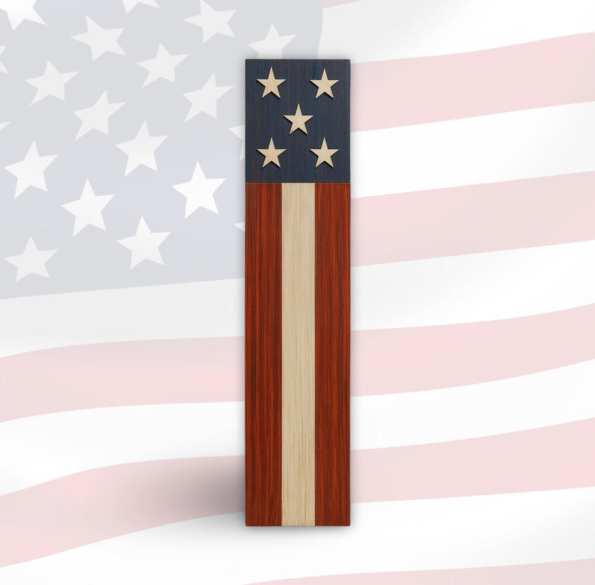 A handcrafted wooden porch sign inspired by the American flag, featuring five carved stars on a navy blue background with vertical red and natural woodgrain stripes, displayed against a faded flag backdrop.
