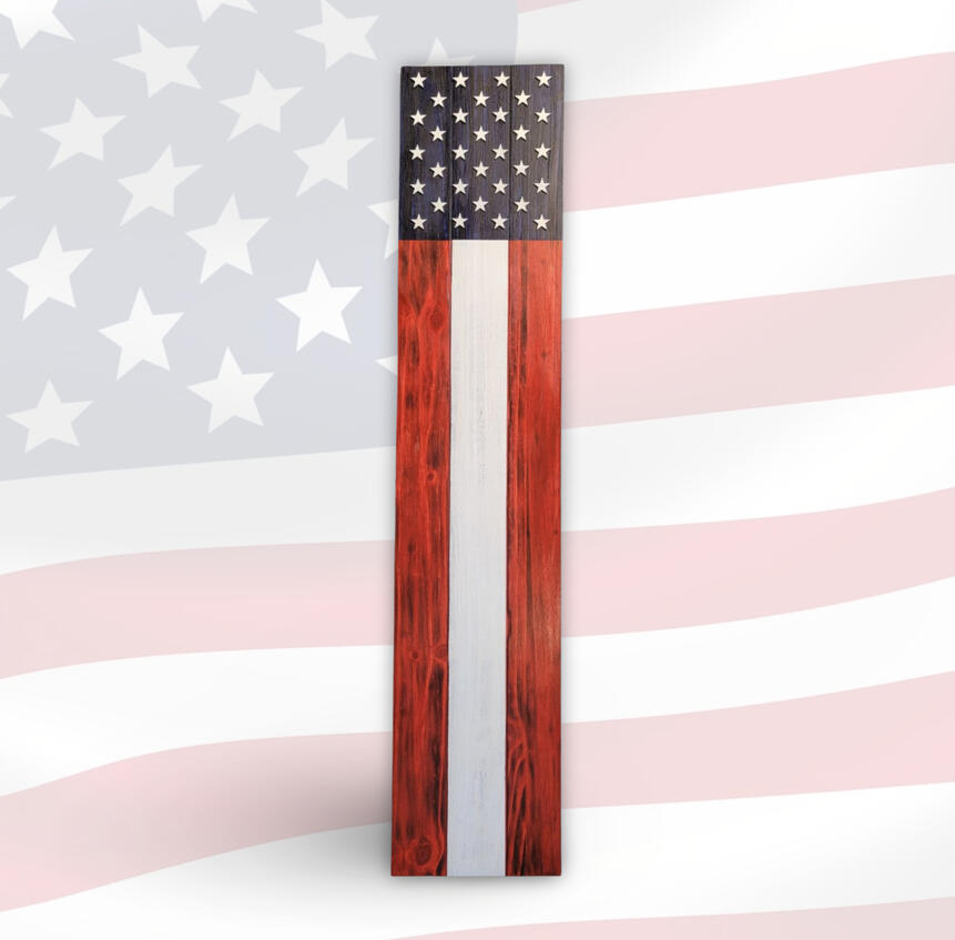 A handcrafted vertical wooden porch sign featuring a navy blue field with multiple carved stars and bold rustic red, white, and natural woodgrain stripes, set against a faded American flag background.